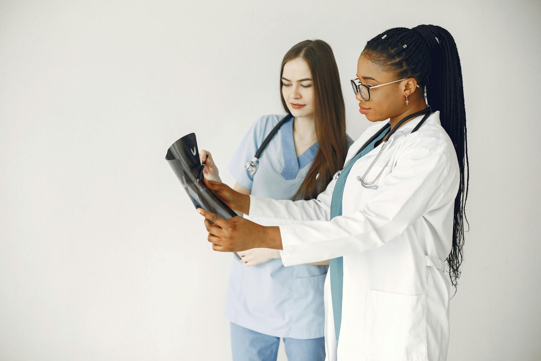 Two healthcare professionals, one in a lab coat and one in scrubs, examine an X-ray image together against a plain white background.